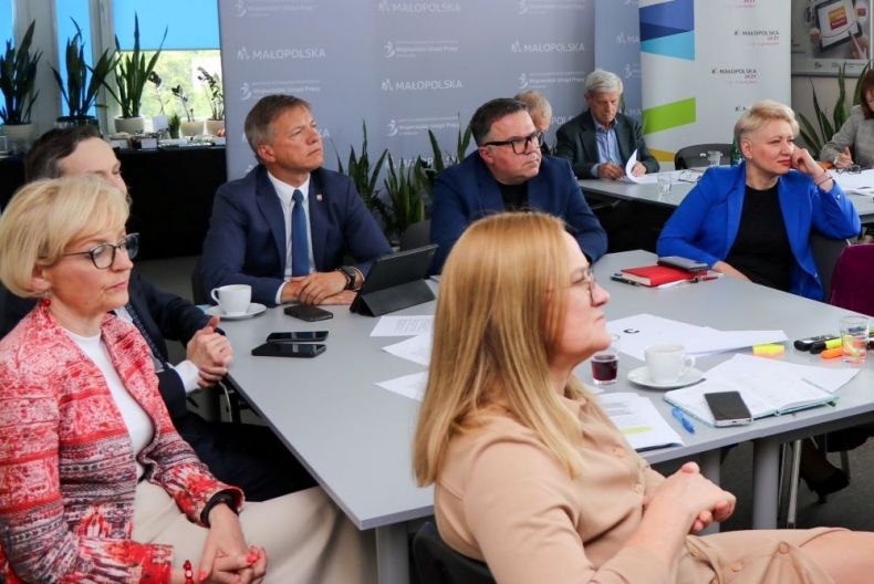 Wojciech Piech siedzi przy stole z innymi ludźmi.