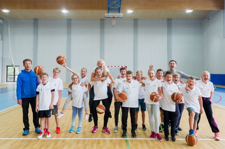 Grupa dzieci w strojach sportowych z piłkami w rękach. 