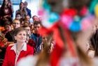 Na pierwszym planie rozmyta postać kobiety w wianku krakowskim, na dalszym planie publiczność