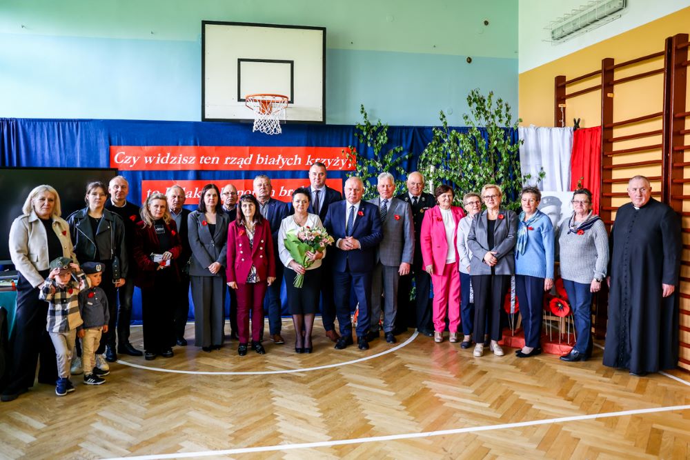 Uczestnicy wydarzenia stoją na sali gimnastycnej w szkole.
