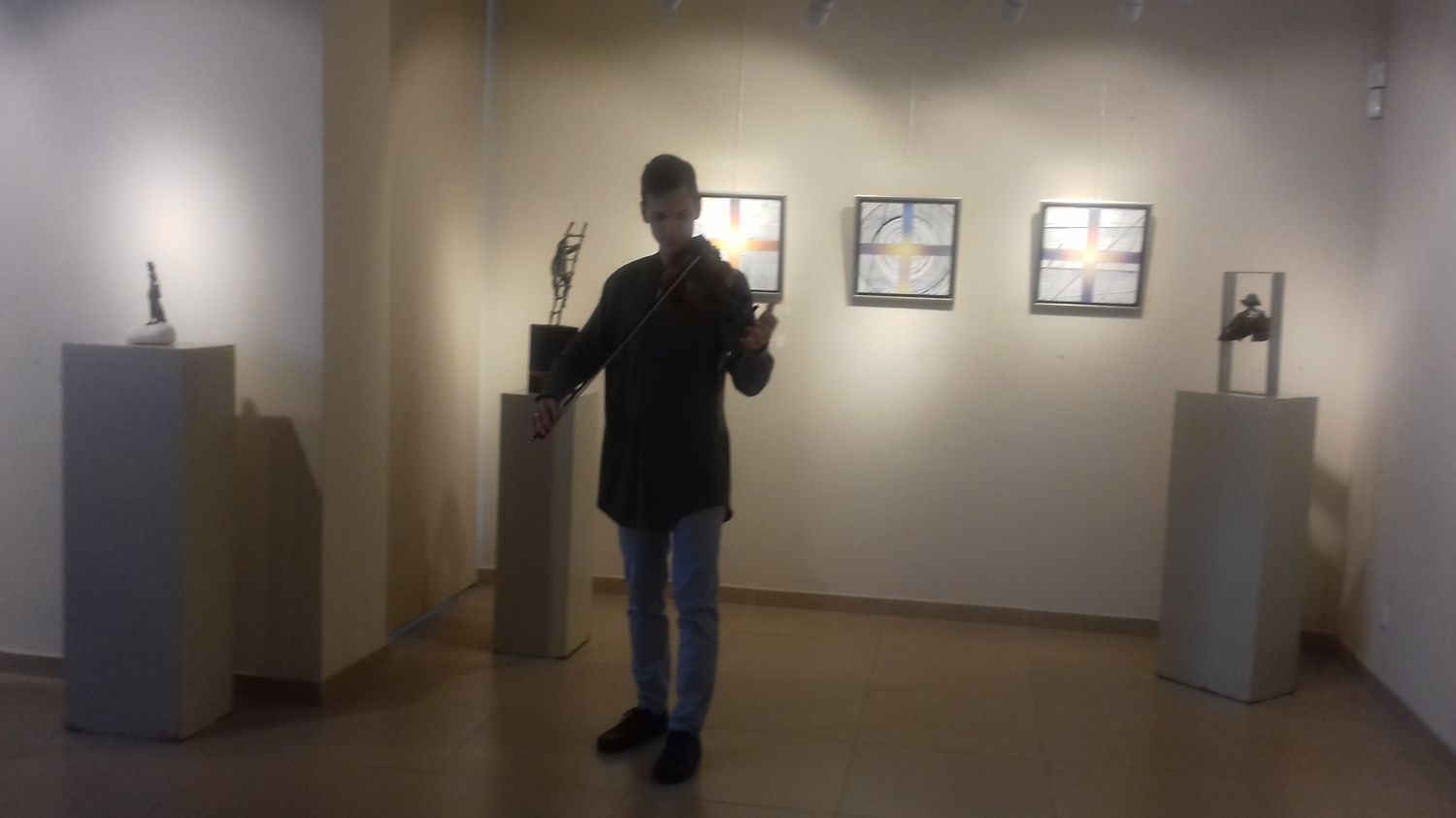 Na zdjęciu skrzypek grający na środku sali wystawienniczej, w tle obrazy na ścianach.