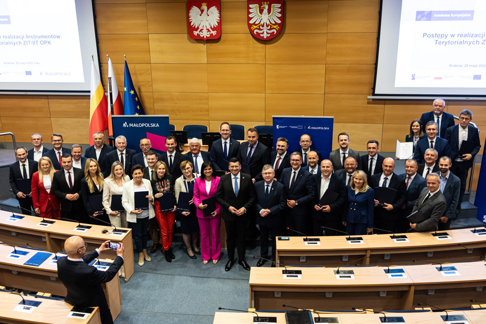 Uczestnicy wydarzenia stoją na sali sesyjnej.