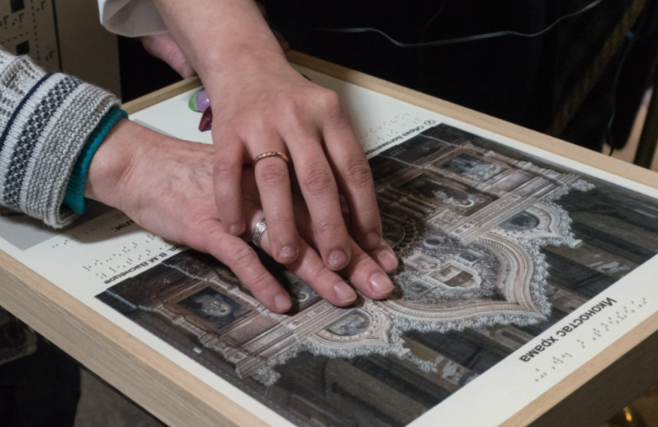 Zdjęcie przedstawia dłonie starszej osoby dotykające eksponat muzealny przystosowany dla osób z dysfunkcją wzroku
