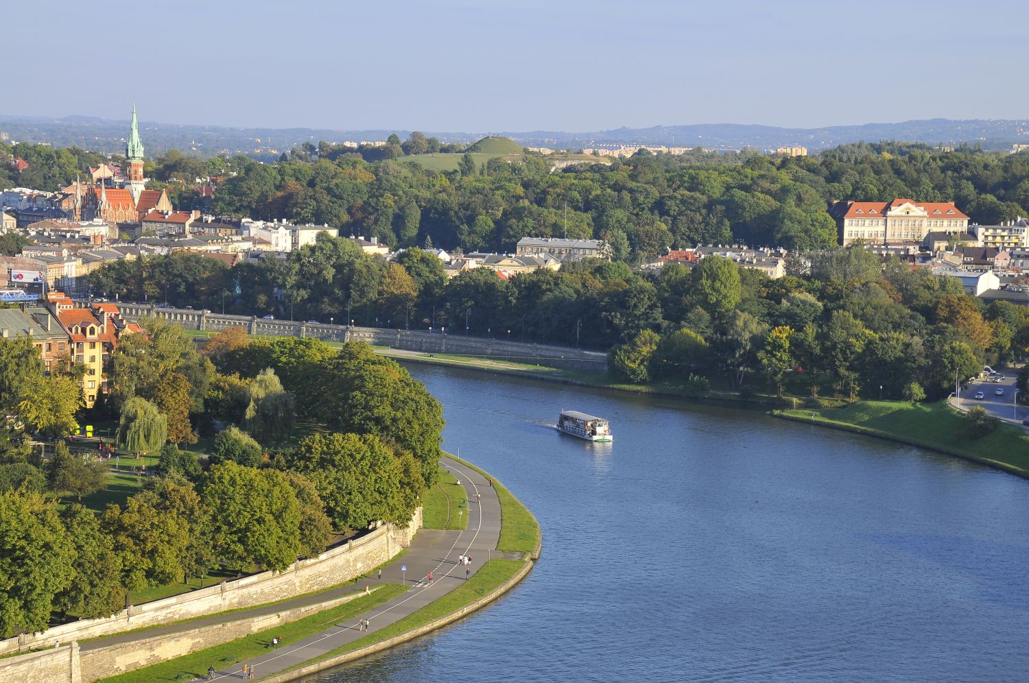 Zdjęcie przedstawia panoramę Krakowa. Na pierwszym planie znajduje sie zakole rzeki Wisły