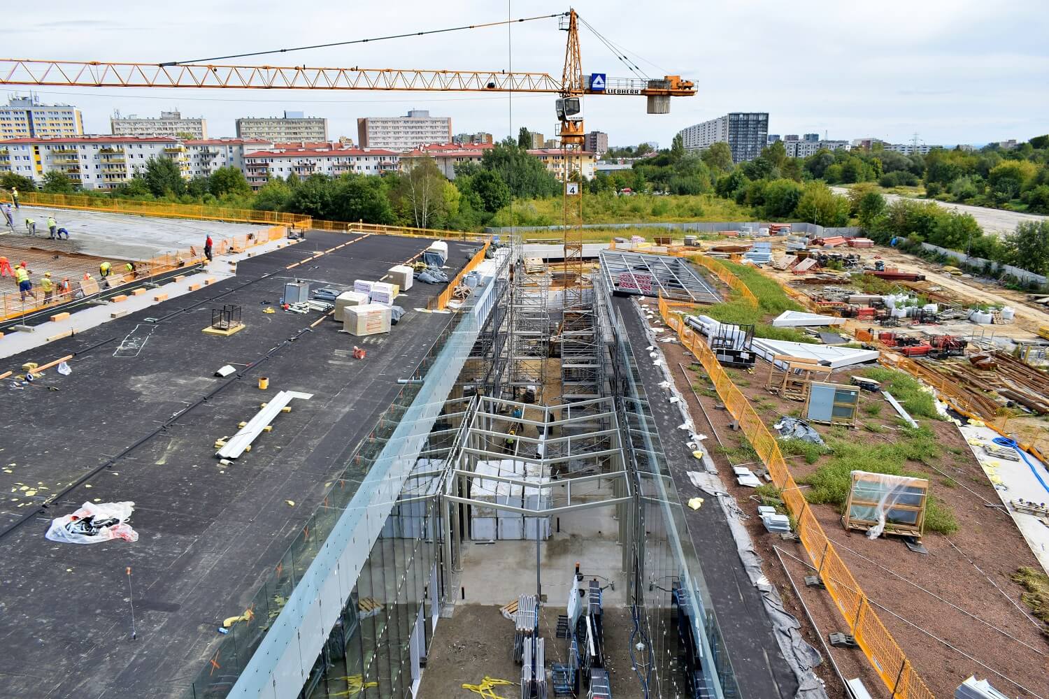 Widok z lotu ptaka na budowę centrum nauki - widać zielony dach, szkielet szklarni, dźwig budowlany