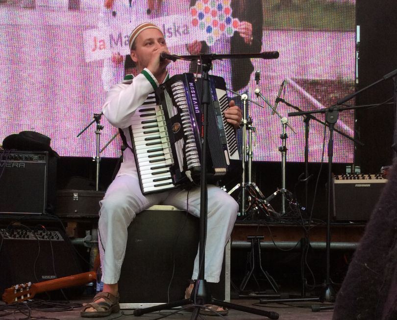 Kolorowe zdjęcie przedstawiające mężczyznę grającego na akordeonie i śpiewającego na scenie